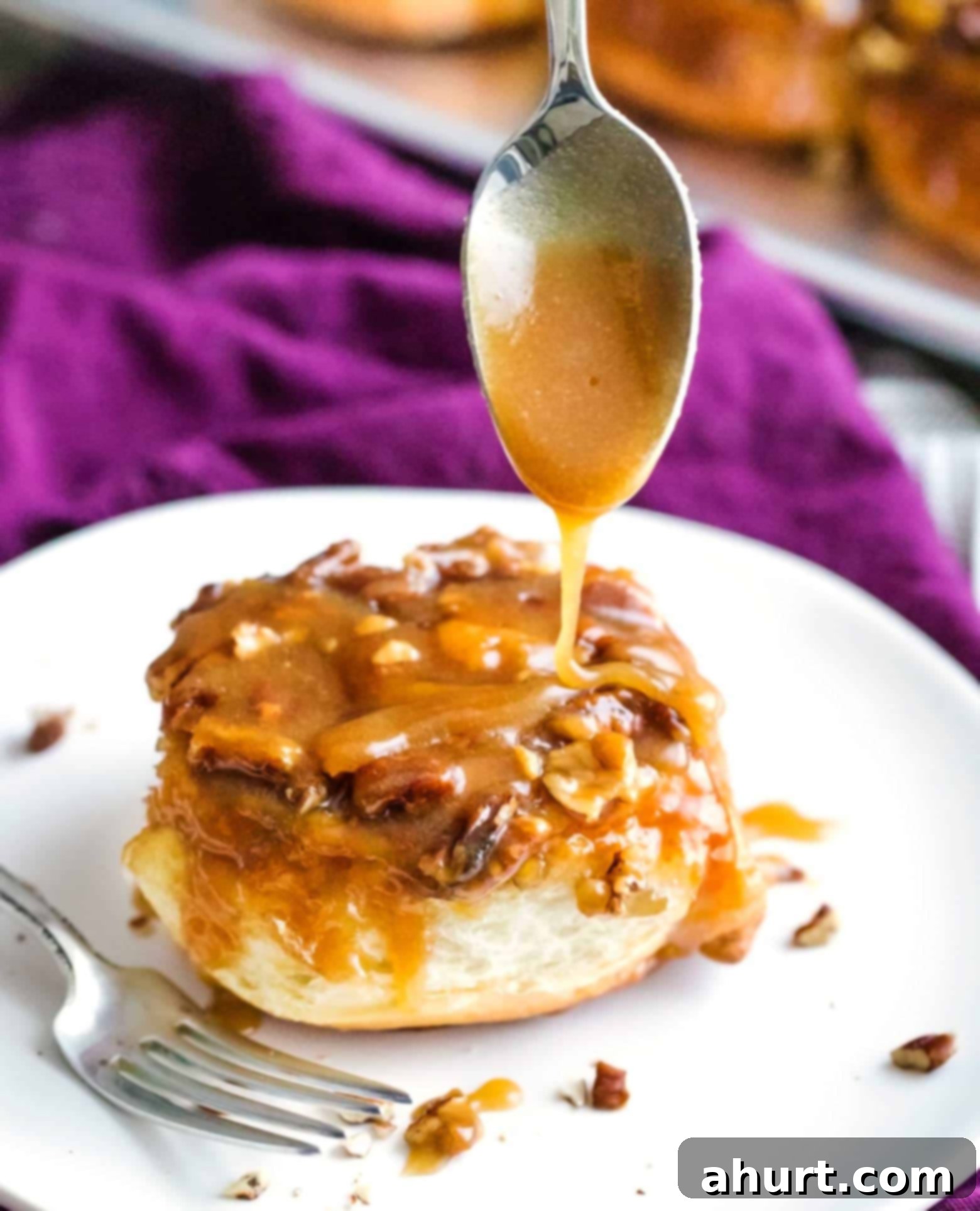 Warm maple syrup being poured over freshly baked pecan sticky buns on a white plate.