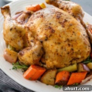The Best Slow Cooker Whole Chicken 6 A full size slow cooked, golden chicken on a bed of roughly chopped carrots, potatoes and herbs, on a white serving platter.