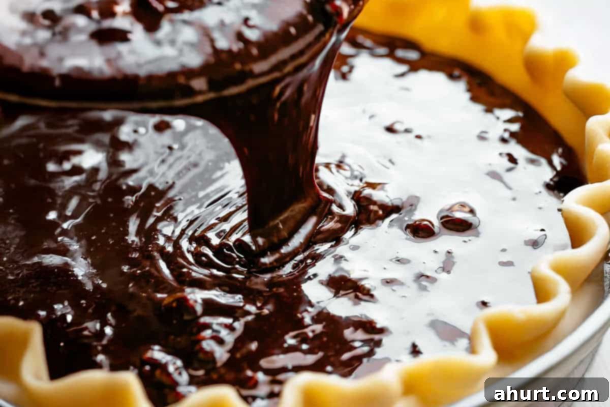 Decadent Chocolate Pecan Pie 7 A rich, gooey chocolate pecan pie mixture being carefully poured into a homemade, golden-brown pie crust, filling it almost to the edge.