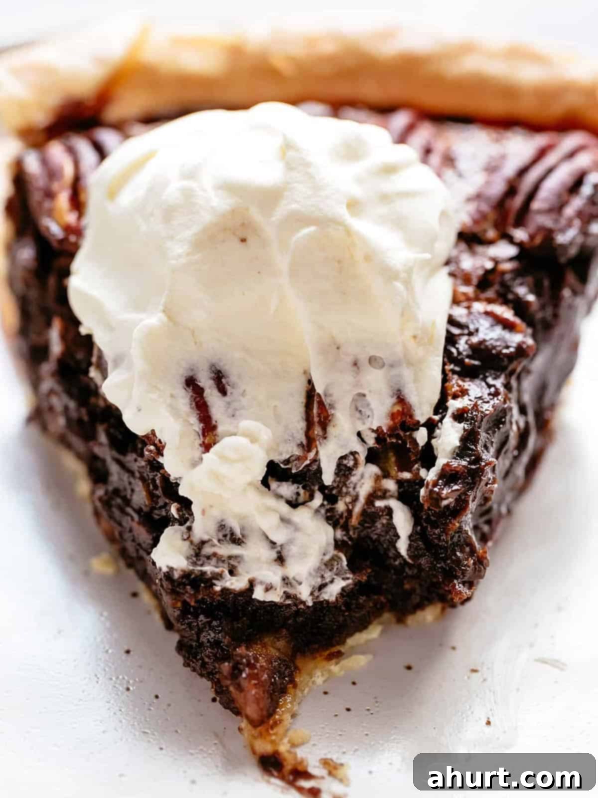 Decadent Chocolate Pecan Pie 10 A perfectly baked, golden-crusted chocolate pecan pie with a dollop of fresh cream on top, with one slice already cut and removed, showcasing the gooey chocolate and pecan filling.