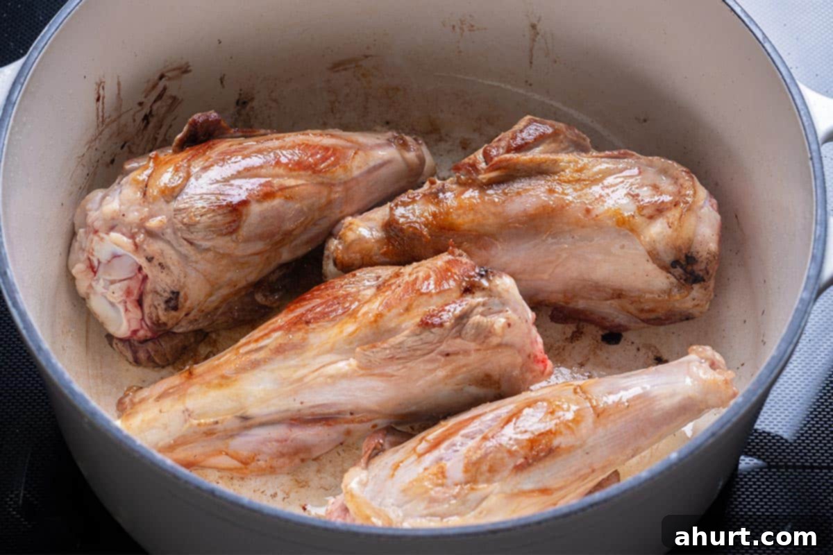Fall-Off-The-Bone Lamb Shanks 5 Lamb shanks searing in a blue pot until deeply browned.