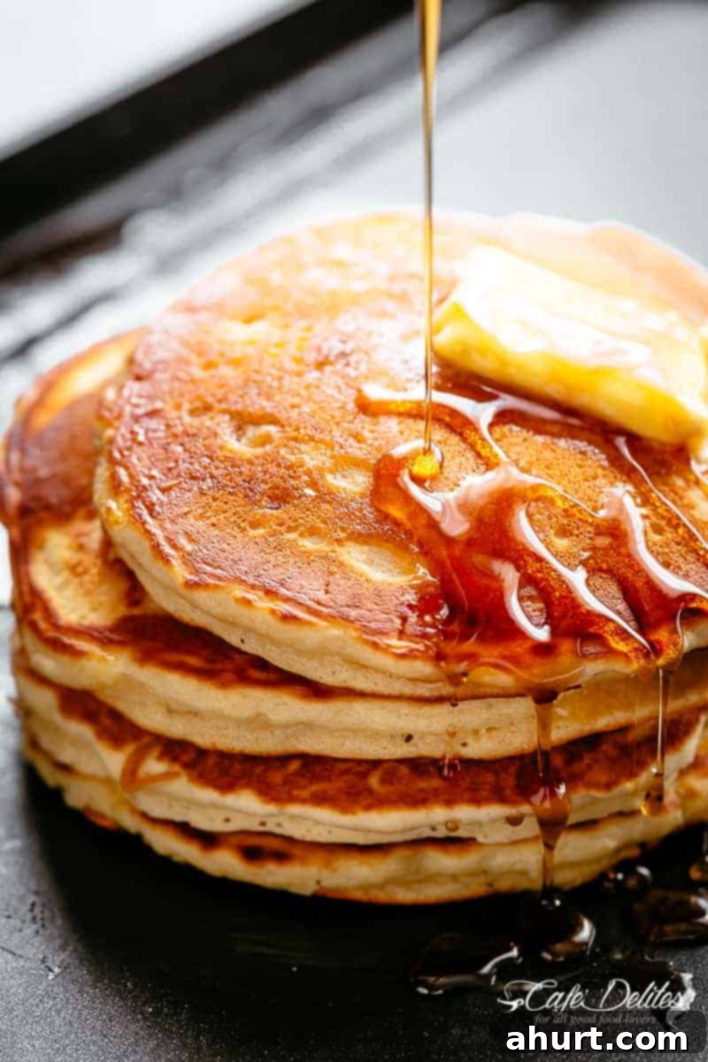 Stack of golden, fluffy buttermilk pancakes drizzled with maple syrup on a white plate, ready for breakfast or brunch. Perfect for a delicious weekend treat.