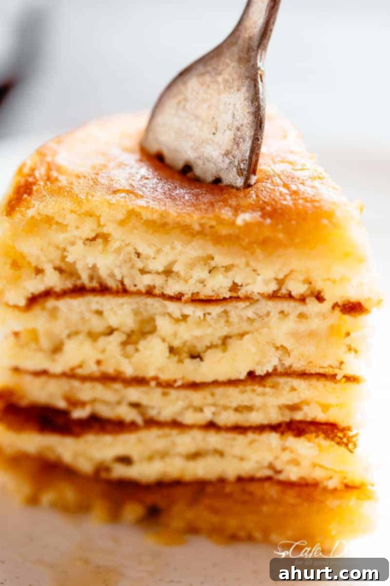 Close-up of a stack of fluffy buttermilk pancakes on a plate, with one piece cut and ready to be eaten, showcasing their tender texture.