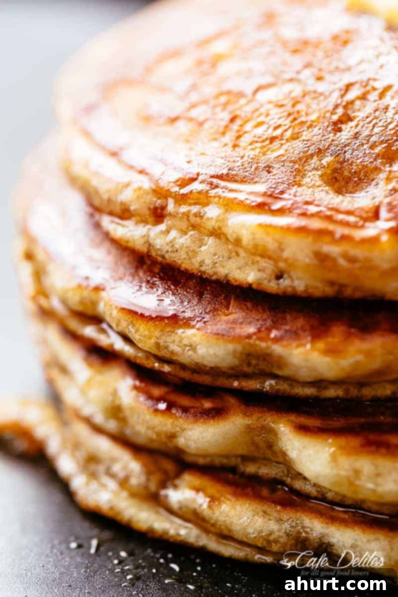 Fluffy buttermilk pancakes with maple syrup dripping down, served on a white plate ready to eat.