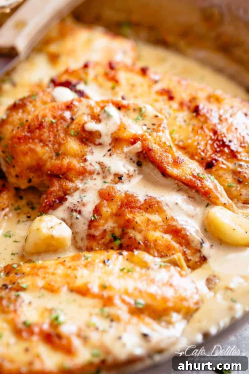 Irresistible Creamy Garlic Chicken Breasts 4 Three golden-brown chicken breasts, coated in a rich, mouth-watering garlic cream sauce, studded with soft, whole garlic cloves, in a skillet.