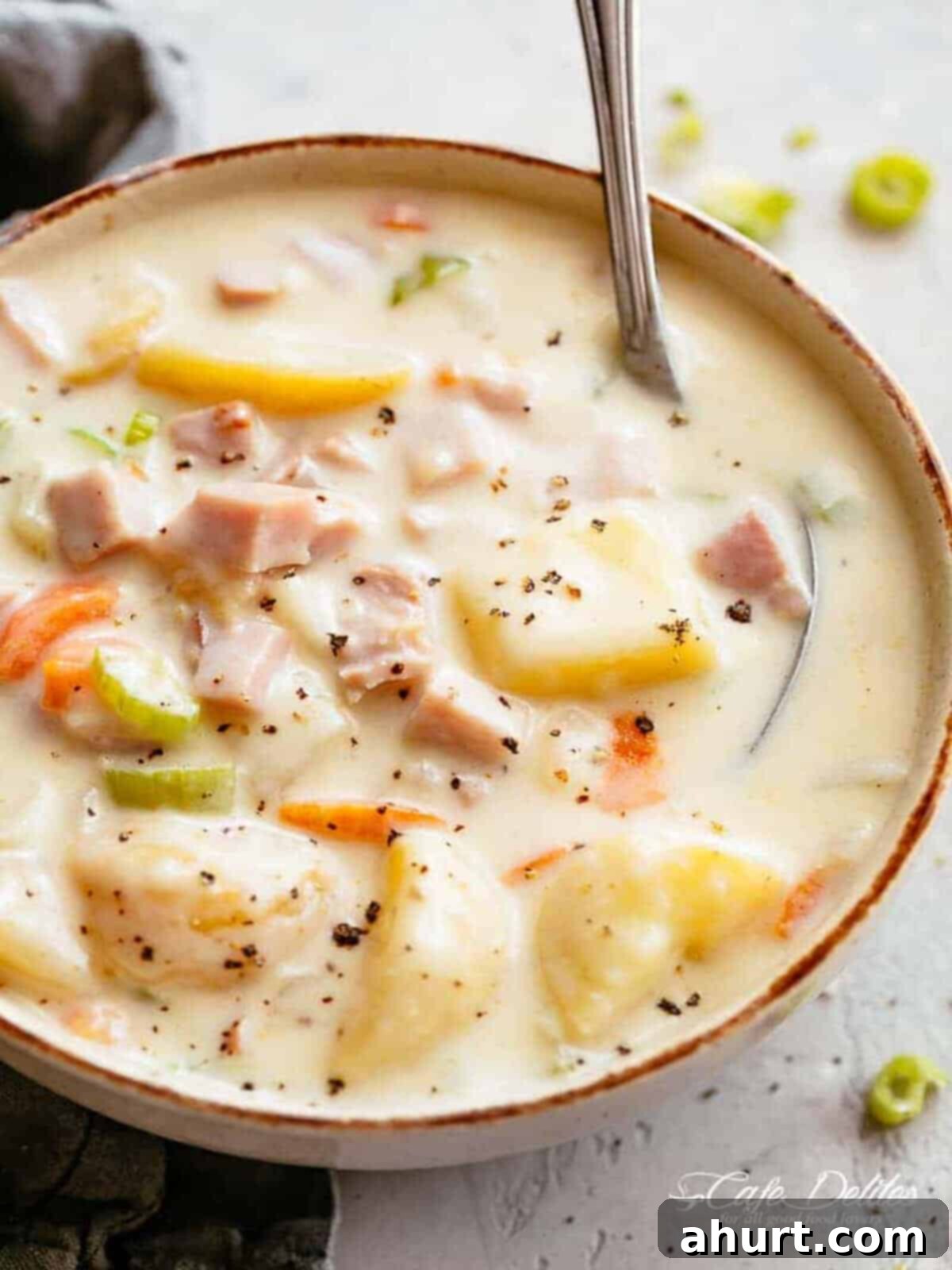 Creamy Ham Potato Soup in a bowl #cafedelites #ham #potato #soup #recipe Image of a scrumptious creamy ham and potato soup with cracked pepper sprinkled on top, being stirred by a spoon.