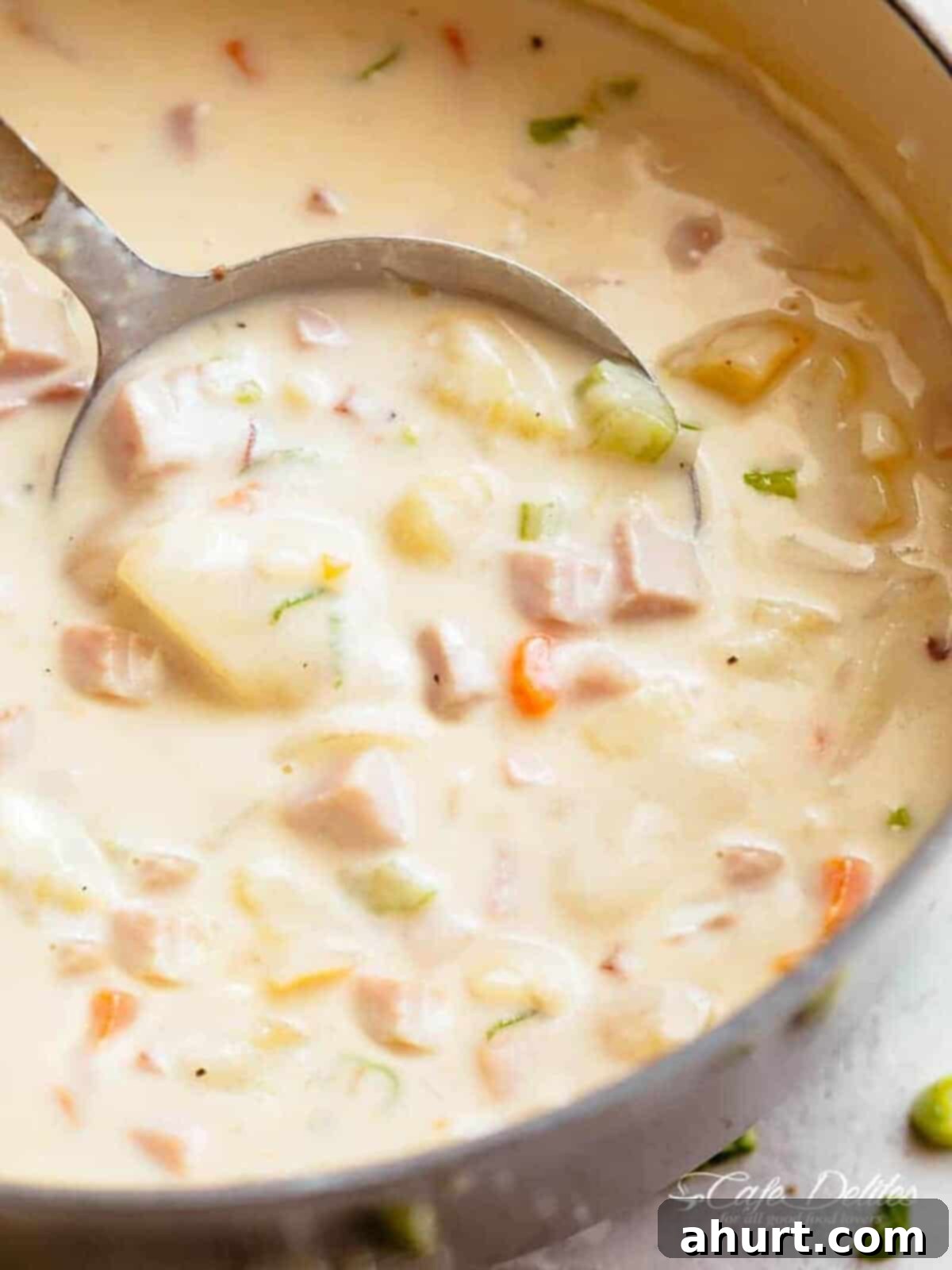 The best Ham and Potato Soup in a pot with a ladle #cafedelites #ham #pot #lecreuset #potatoes Image of creamy ham and potato soup being scooped up by a spoon, ready to be enjoyed.