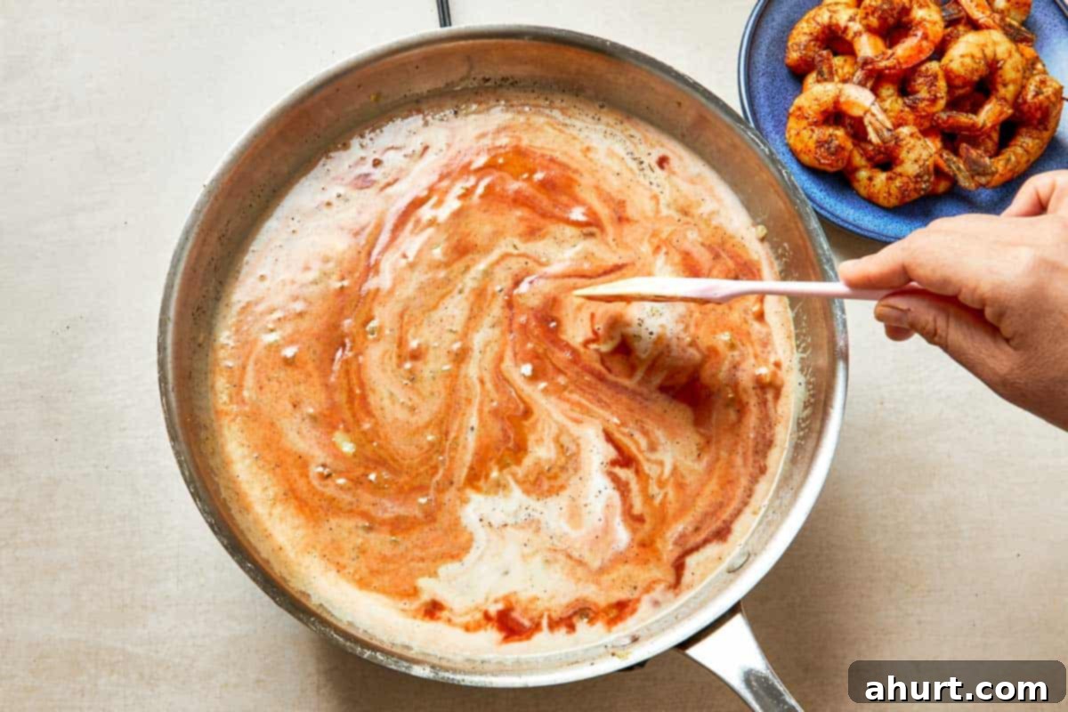 Easy Creamy Coconut Shrimp Curry 8 Hand stirs shrimp in a pan with a thickening sauce of crushed tomatoes, coconut milk, and chili powder.