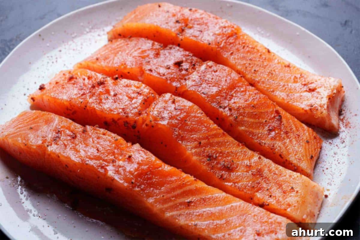 Spicy Firecracker Salmon 4 Image of beautifully laid-out salmon fillets being seasoned generously with salt, black pepper, and paprika on a white circular plate.