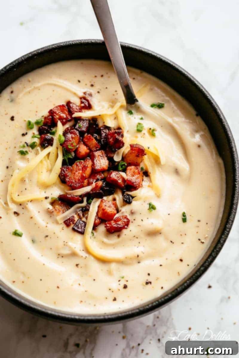A bowl of Cauliflower soup. Low carb and Keto recipe #cafedelites #cauliflowersoup #cauliflower #lowcarb #Keto #bacon #cheese Thick and Creamy Cauliflower Soup is a delicious, healthy low carb substitute for potato soup! Blended with cream and served with crispy bacon, chives and shredded cheese in a bowl
