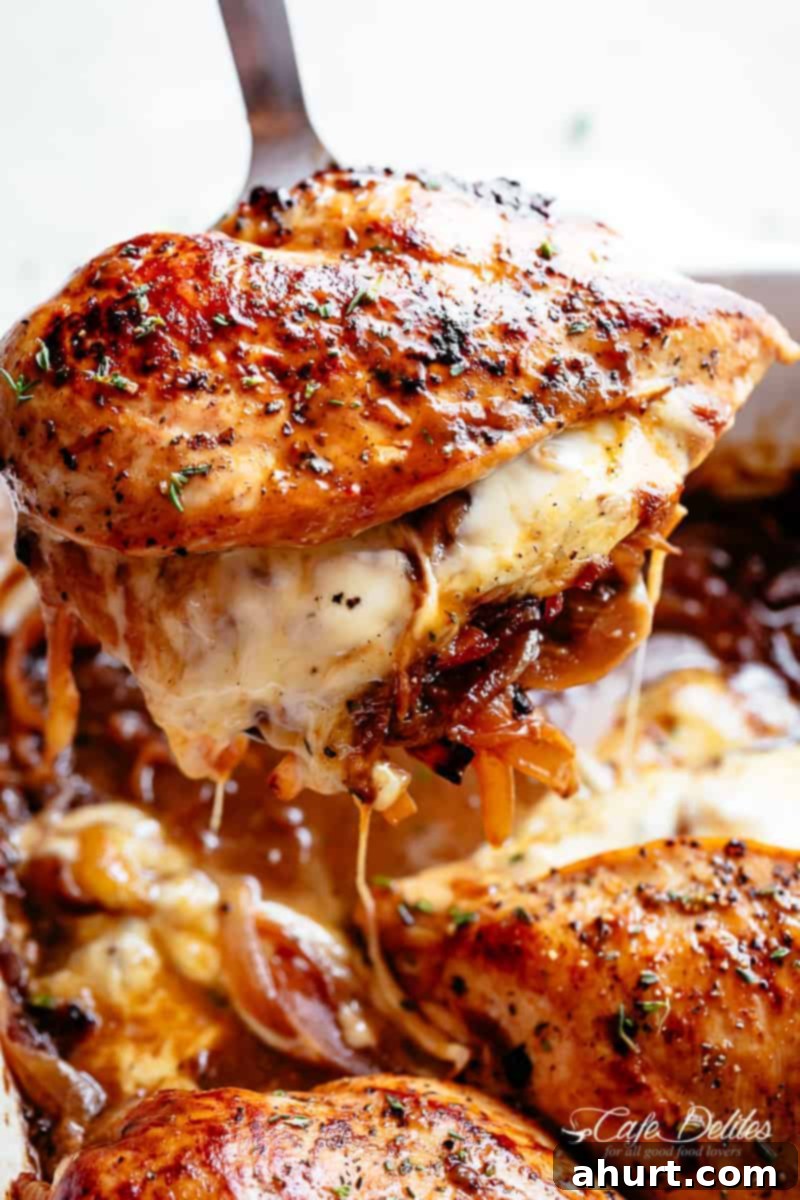 Stuffed chicken with French onion sauce and melted cheese #cafedelites #chicken French Onion Stuffed Chicken piece being pulled out of casserole, showcasing melted cheese and onions