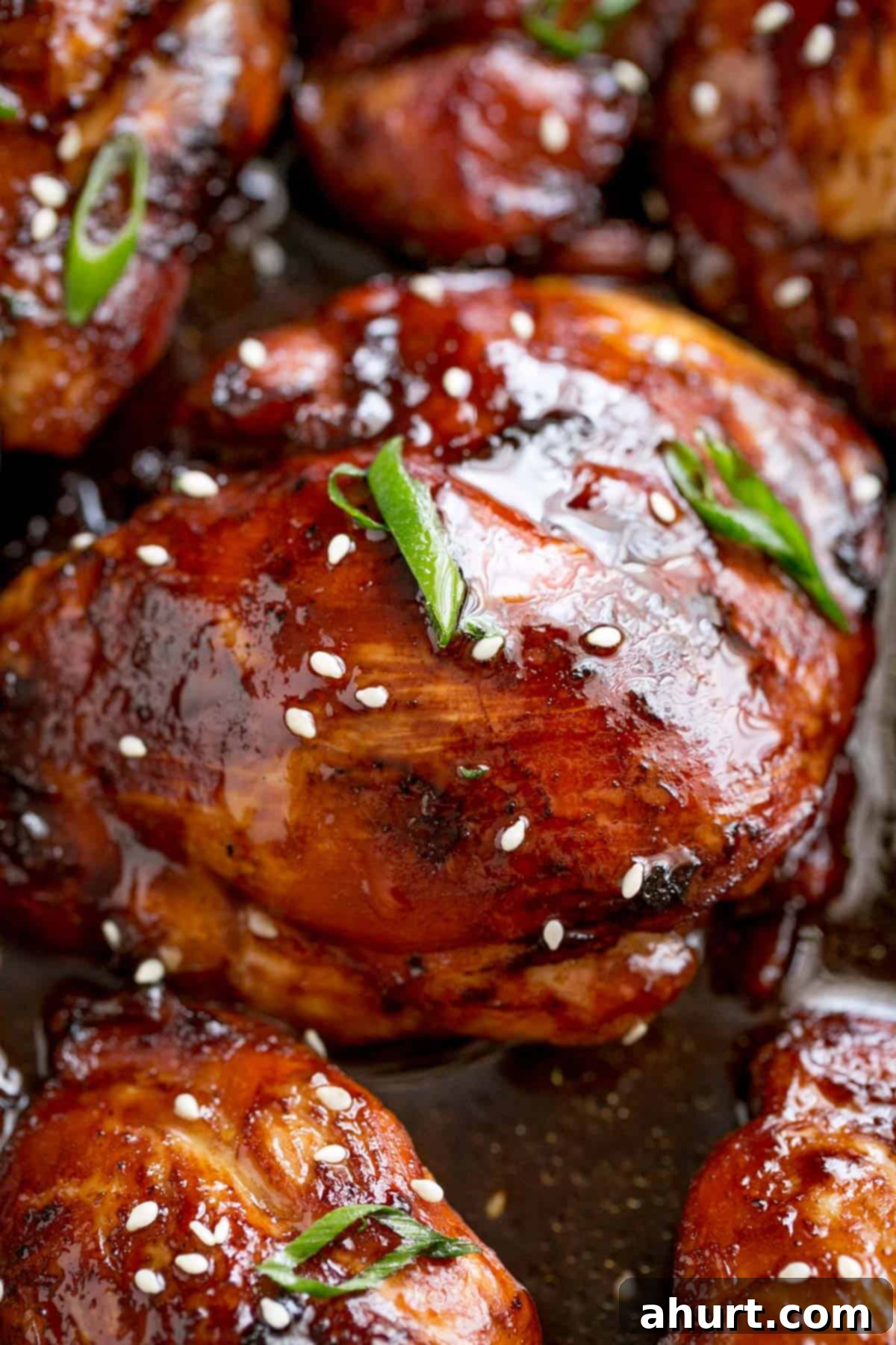 Honey Soy Glazed Chicken Thighs 10 A close-up image of an oven-baked chicken thigh glazed with honey soy sauce and garnished with sesame seeds and scallions.