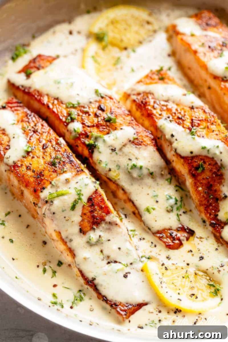 Decadent Garlic Butter Salmon 10 Four soft salmon fillets sitting and covered in creamy garlic butter sauce. Fresh herbs and two lemon wedges are scattered across the top of the fish.
