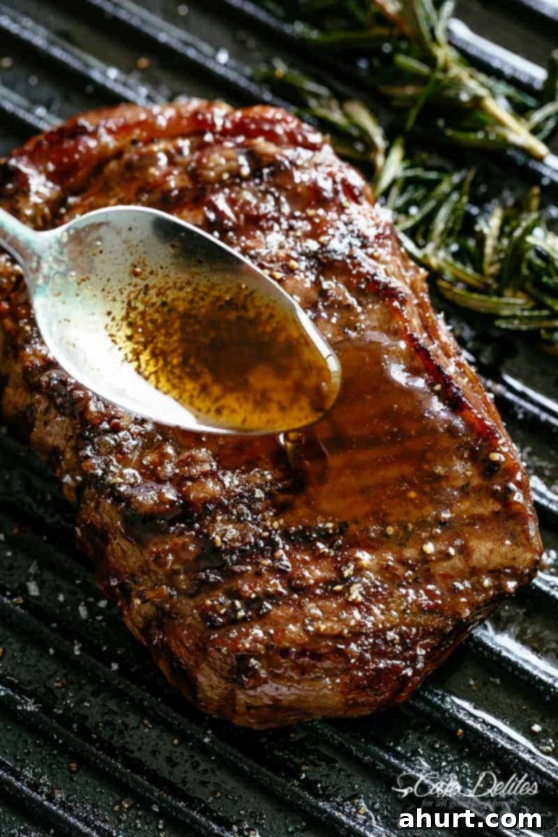 Silver spoon drizzling garlic browned butter over a juicy grilled steak with rosemary on a black grill pan, showcasing a perfect sear and glistening finish.