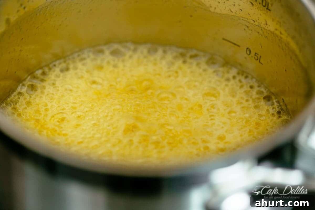 Foaming golden melting butter in a silver pot on a grill, indicating the initial stage of browning.