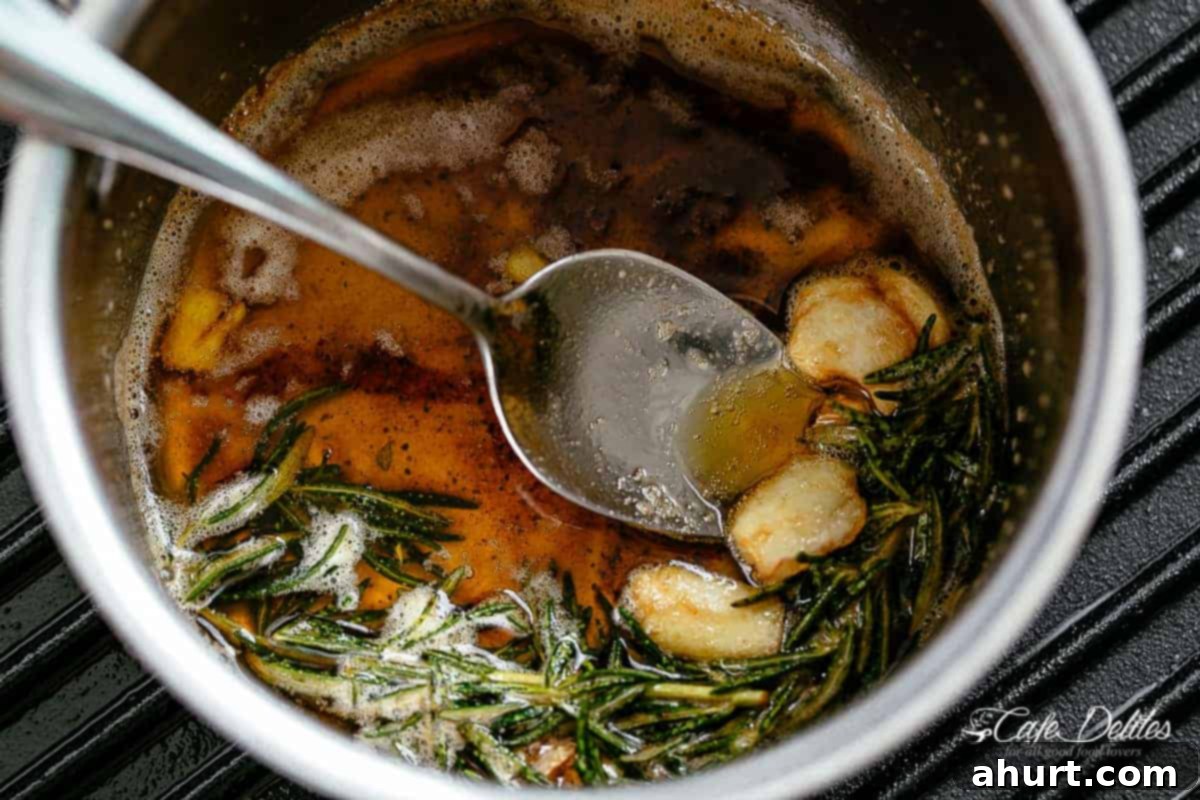 Image of perfectly browned butter with crushed garlic cloves and sprigs of fresh rosemary infusing in a silver pot on a grill pan, ready to sauce the steaks.