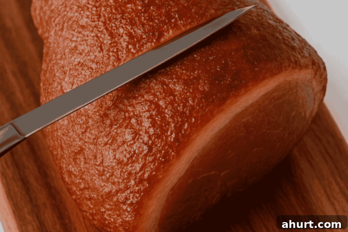 Caramelized Maple Ham 4 Close-up of a ham shank being precisely scored with a sharp knife to create a starting point for rind removal.