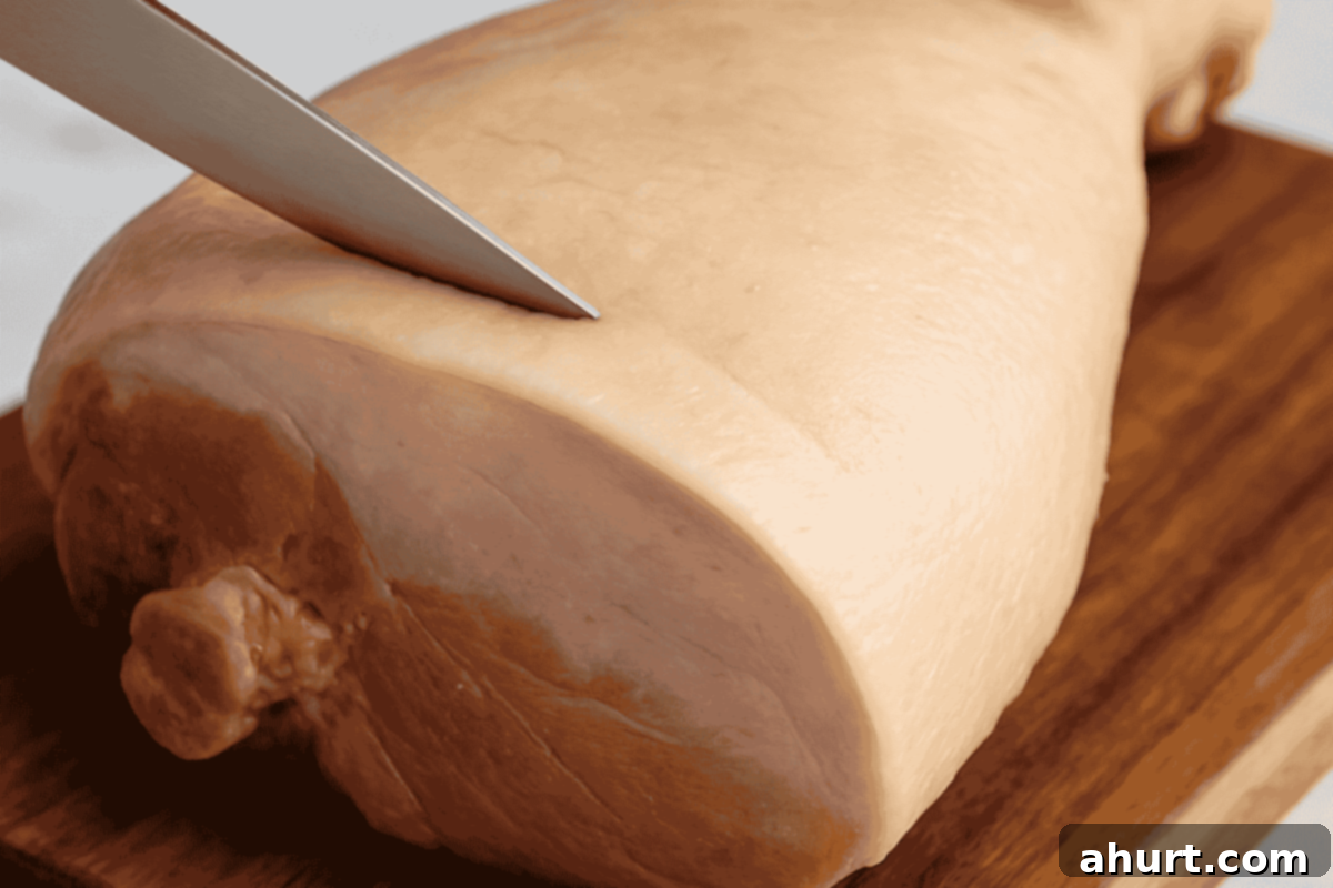 Caramelized Maple Ham 6 A chef's knife smoothing and trimming the fat layer on a ham to create a clean, even surface.