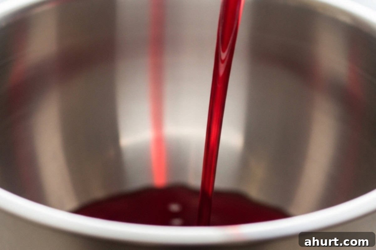 Festive Holiday Punch 4 Pouring cranberry juice into a large steel punch bowl as the first step for Holiday Punch