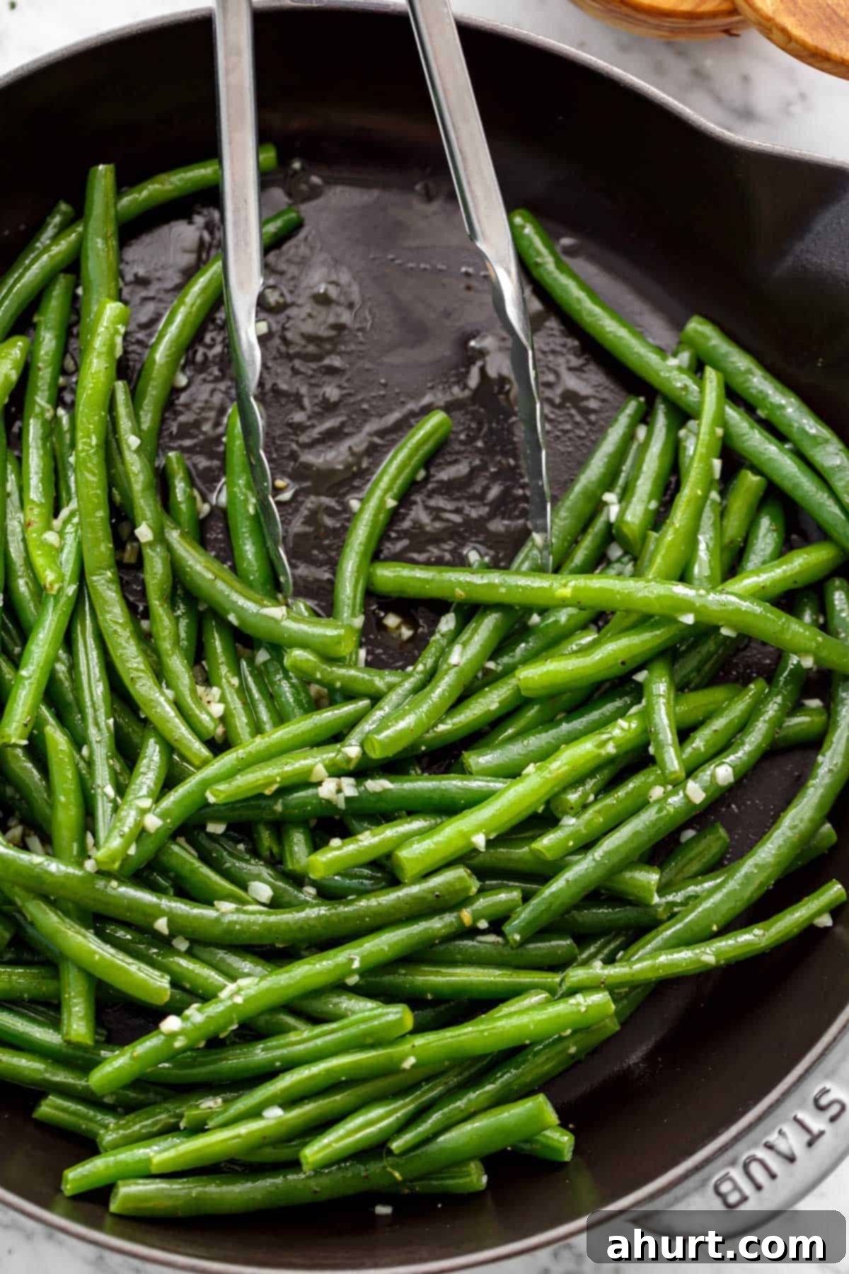 Sautéed, buttery green beans covered in garlic with tongs leaning on side of pan.
