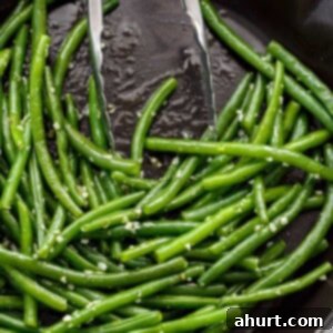 Perfectly Buttery Sautéed Green Beans 5 Sautéed, buttery green beans covered in garlic with tongs leaning on side of pan.