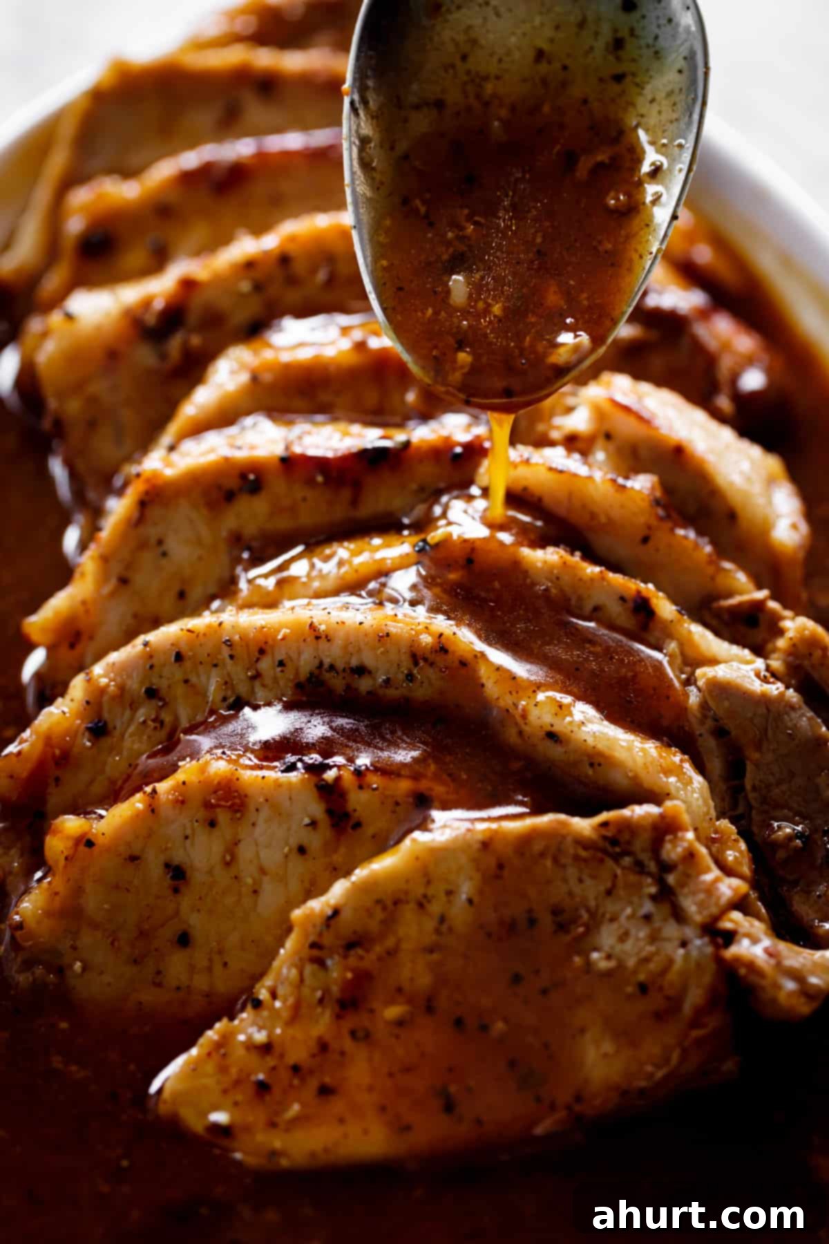 pork loin #roast #pork #loin #recipe Side view of thick brown gravy being poured over thick slices of pork loin roast with a large silver tablespoon.