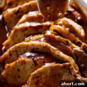 Tender & Juicy Oven-Roasted Pork Loin 12 Side view image of A thick brown gravy being poured over thick slivers of pork loin roast with a large silver tablespoon.