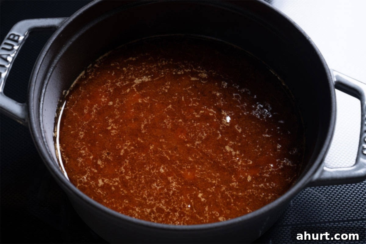 Tender & Juicy Oven-Roasted Pork Loin 8 Pan juices being poured from a slow cooker into a pot for sauce preparation.