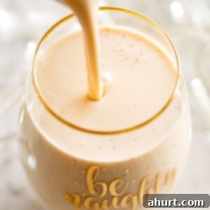 Best Creamy Eggnog Recipe 10 pouring eggnog into a fancy glass cup, garnished with nutmeg