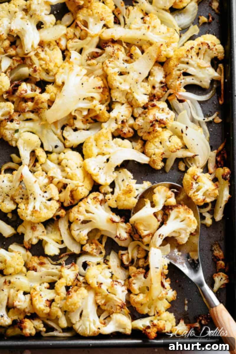 Roasted cauliflower on a baking sheet #cauliflower #roasted #oven Top view of golden roasted cauliflower florets with caramelized onions and garlic on a baking tray, garnished with fresh herbs.