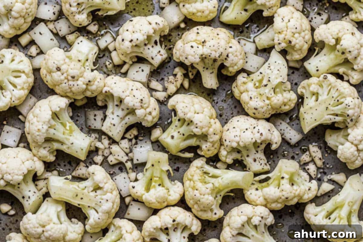 Roasted Cauliflower 5 Olive oil being drizzled over cauliflower, onion, and garlic, then sprinkled with salt, crushed red pepper, and cracked black pepper.