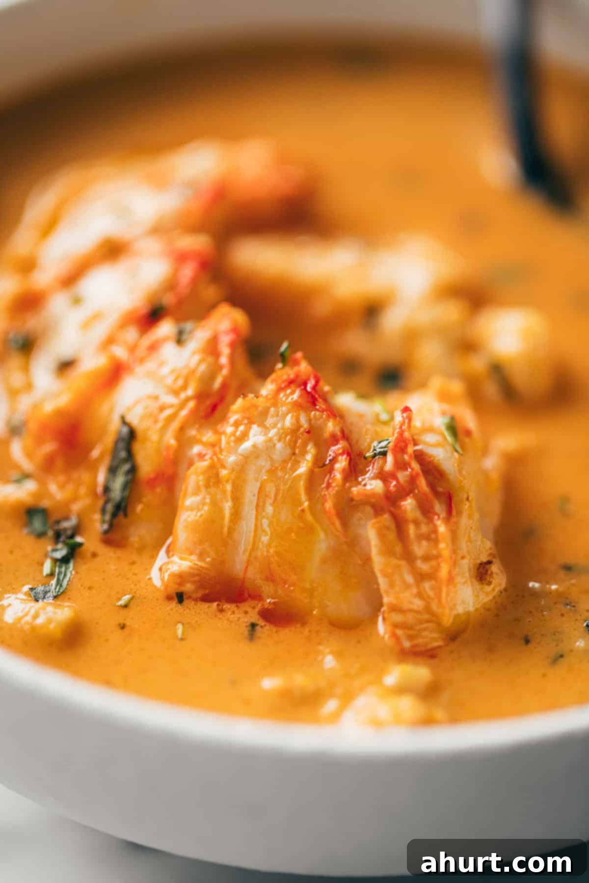 Luxurious Lobster Bisque 15 A mesmerizing close-up image of the rich, creamy lobster bisque, generously topped with succulent chunks of lobster and a sprinkle of fresh herbs, ready to be enjoyed.