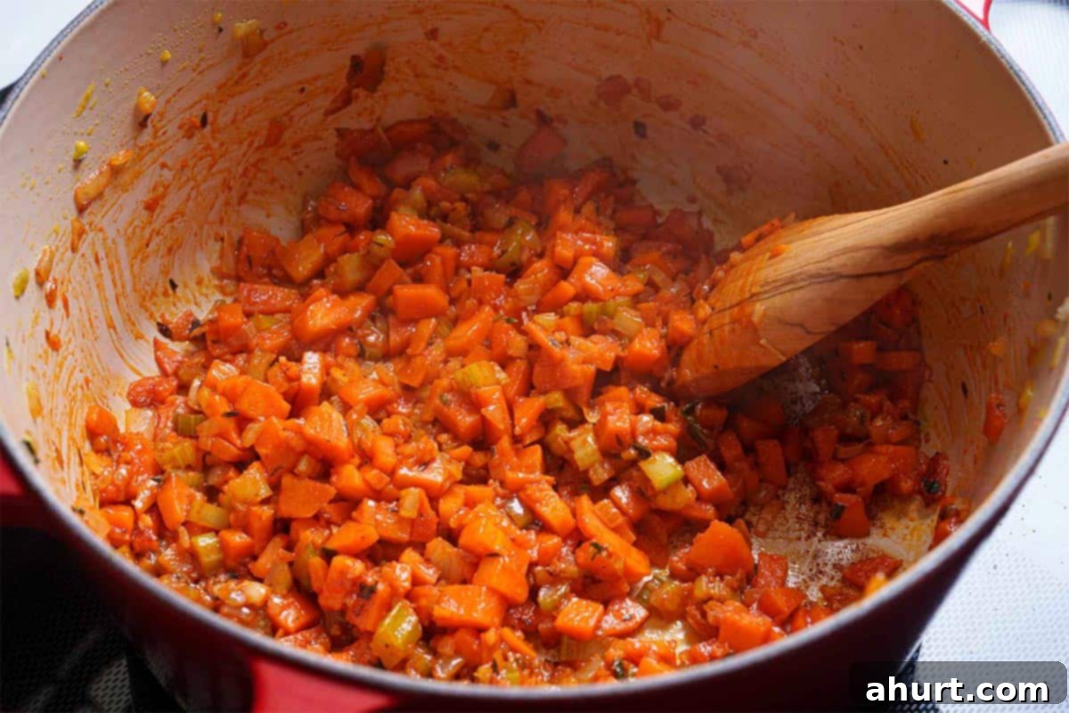 Luxurious Lobster Bisque 9 Sautéed vegetables in a pan, with the addition of rich tomato paste being stirred in to coat them evenly, forming a flavorful base.