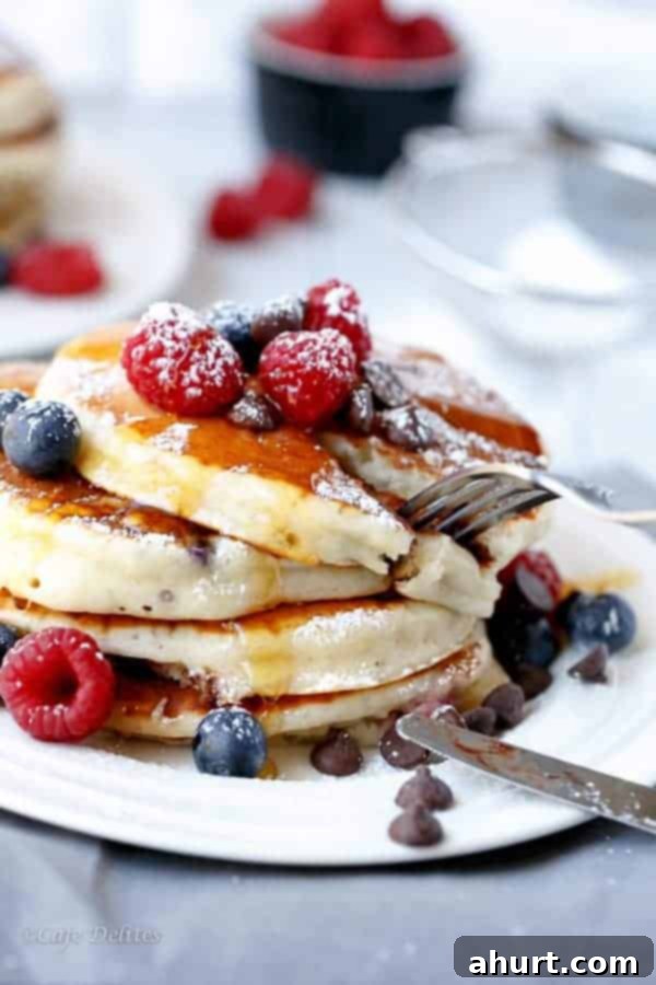 Greek Yogurt Berry Chocolate Chip Cloud Cakes 3 Close-up of a towering stack of Fluffy Greek Yogurt and Mixed Berry Chocolate Chip Pancakes, showcasing their perfect rise and scattered berries.