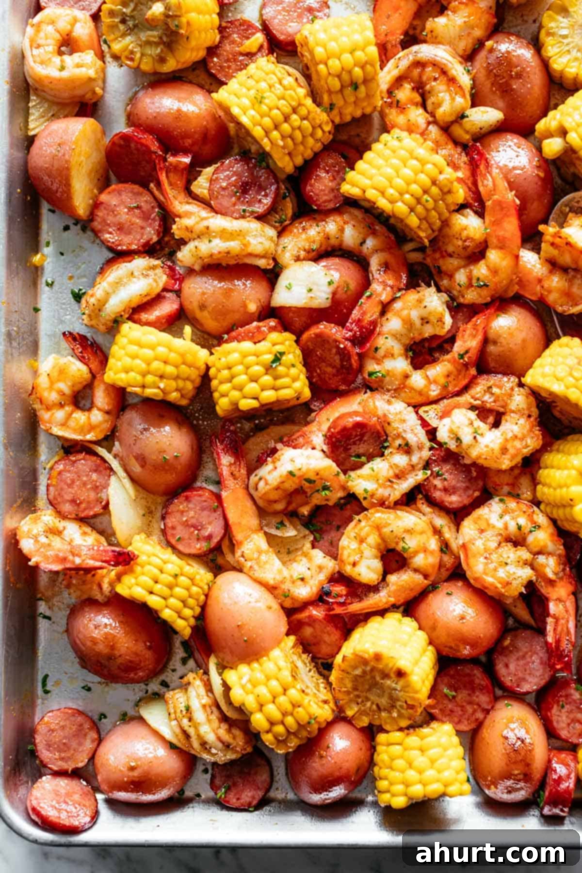 Shrimp boil in the oven with old bay #shrimpboil #cajun #oldbay Shrimp Boil smothered in garlic butter mixture and Old Bay seasoning with chunks of red potatoes and corn on the cob on a silver tray.