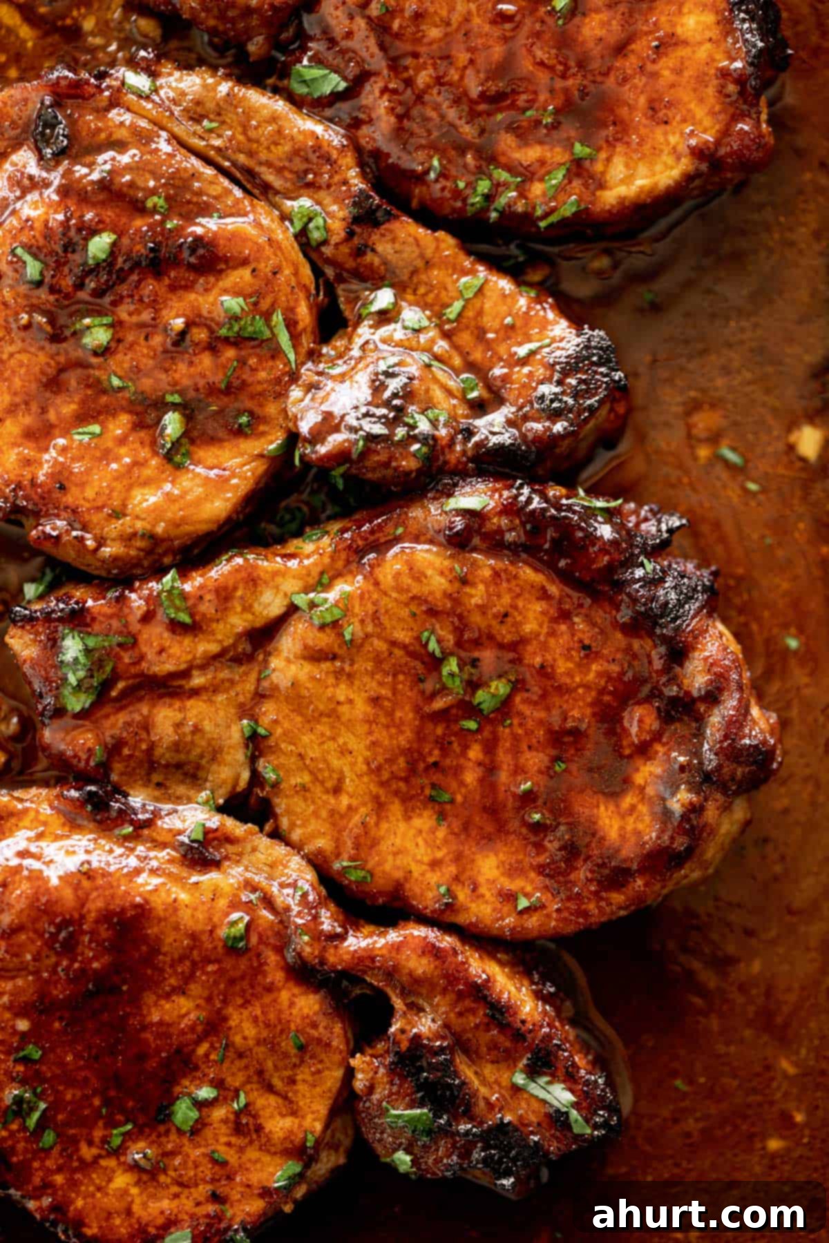 Tender Baked BBQ Pork Chops 2 Oven Baked BBQ Pork Chops on a baking tray, garnished with fresh herbs.