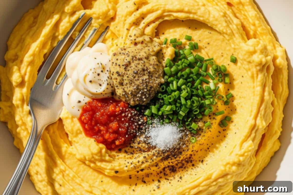 Timeless Deviled Eggs 8 Mashed yolks combined with mayonnaise, Dijon mustard, Tabasco, salt, pepper, and chopped chives in a mixing bowl.