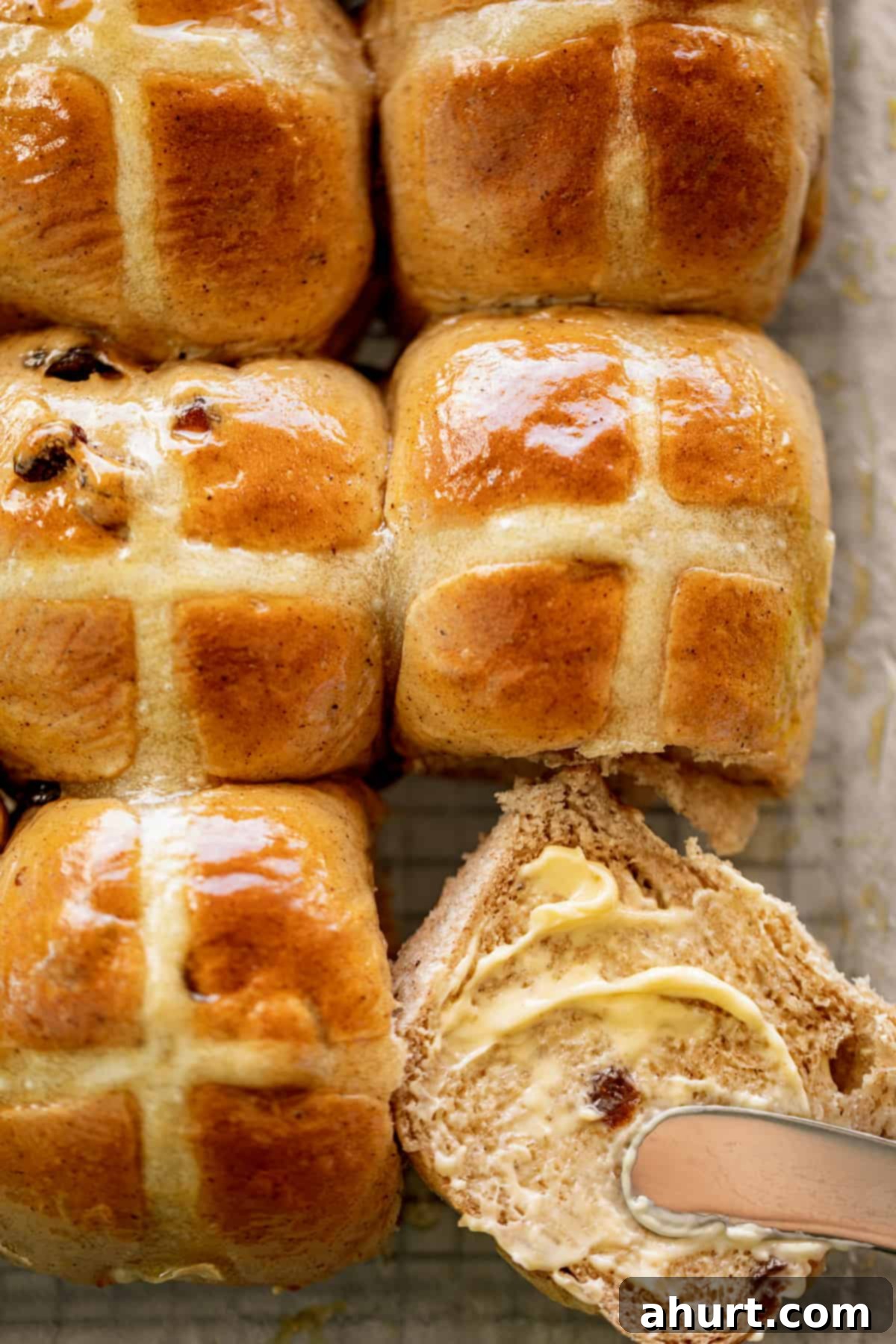 Spiced Easter Indulgence 2 Hot and fluffy Hot Cross Buns with one cut in half and smeared with fresh butter.
