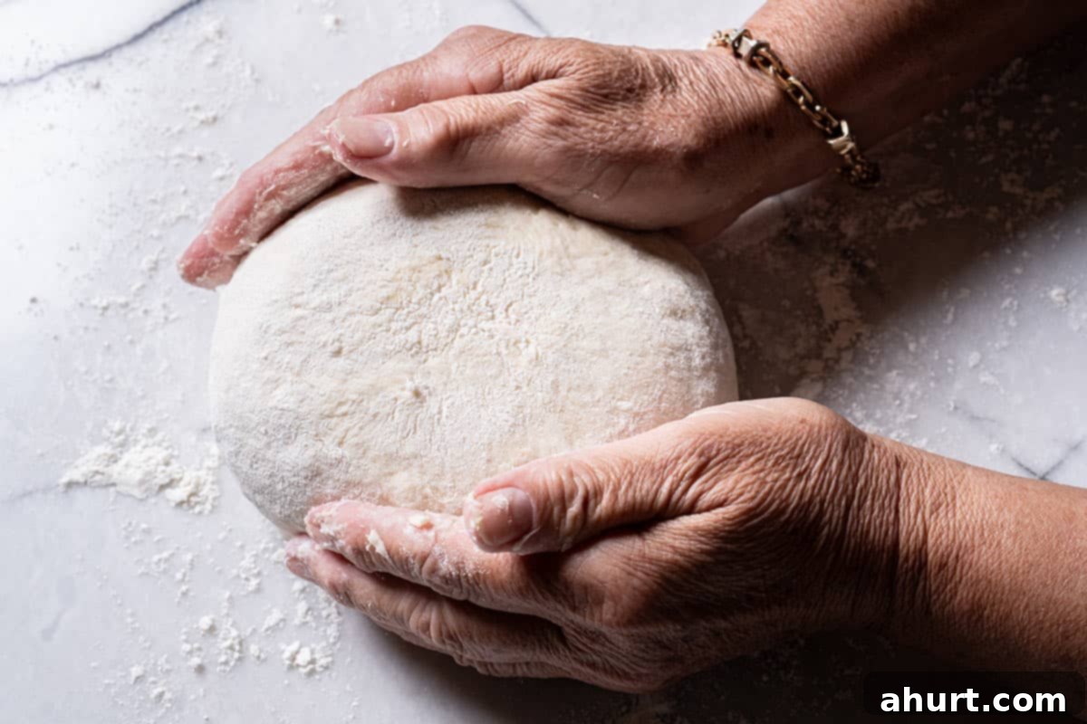 Effortless Artisan Crust: No-Knead Perfection 11 Image of hands turning the though into a well-rounded shape.