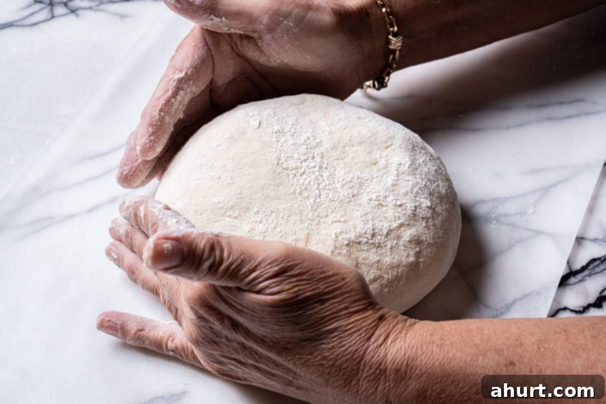 Effortless Artisan Crust: No-Knead Perfection 12 Image of hands moving the round bread dough onto parachment paper.