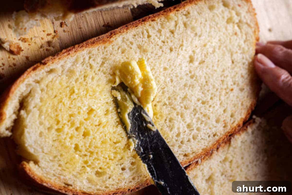 Effortless Artisan Crust: No-Knead Perfection 17 An image of a knife spreading butter over sliced warm bread.