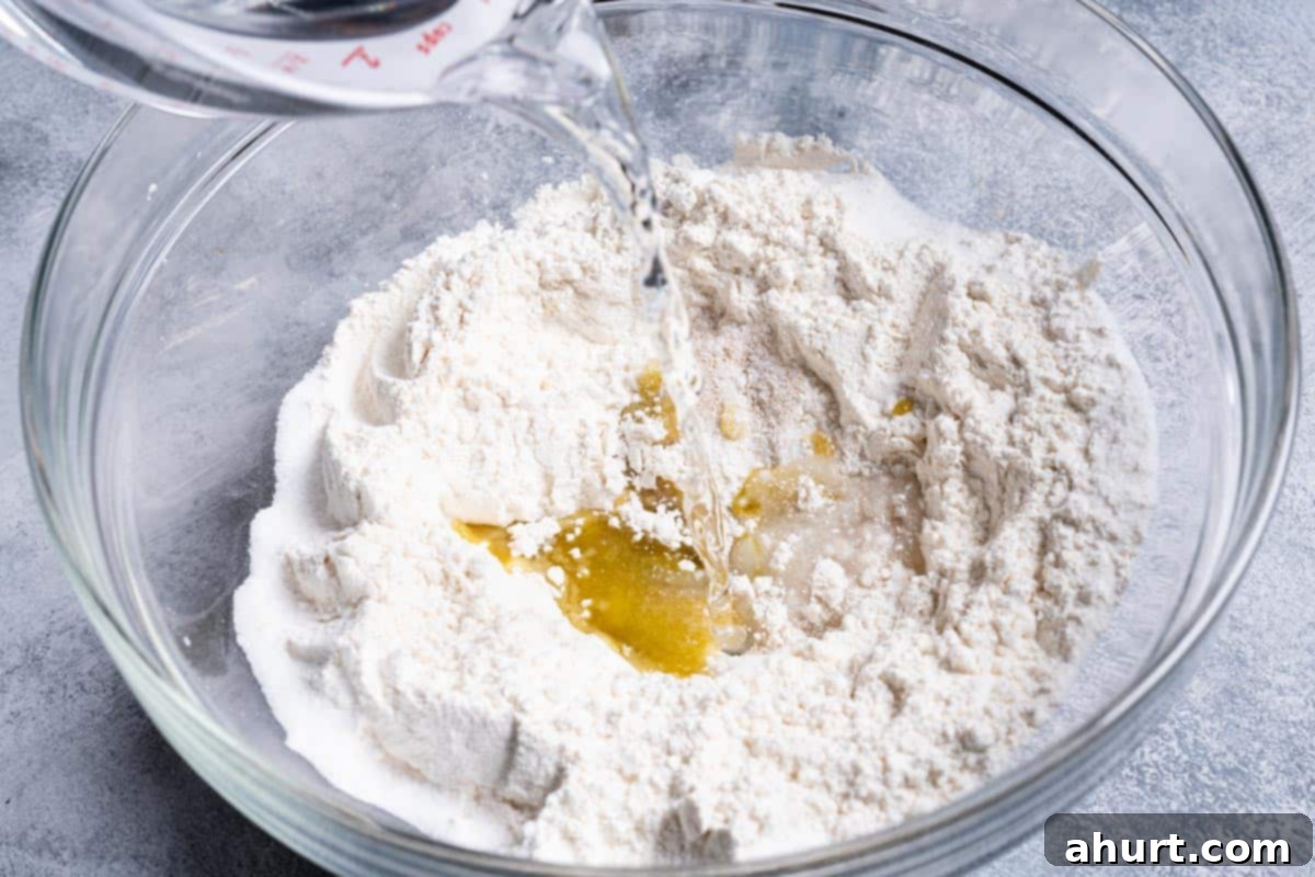 Effortless Artisan Crust: No-Knead Perfection 4 An image of water being added to a clear bowl containing all the ingredients.