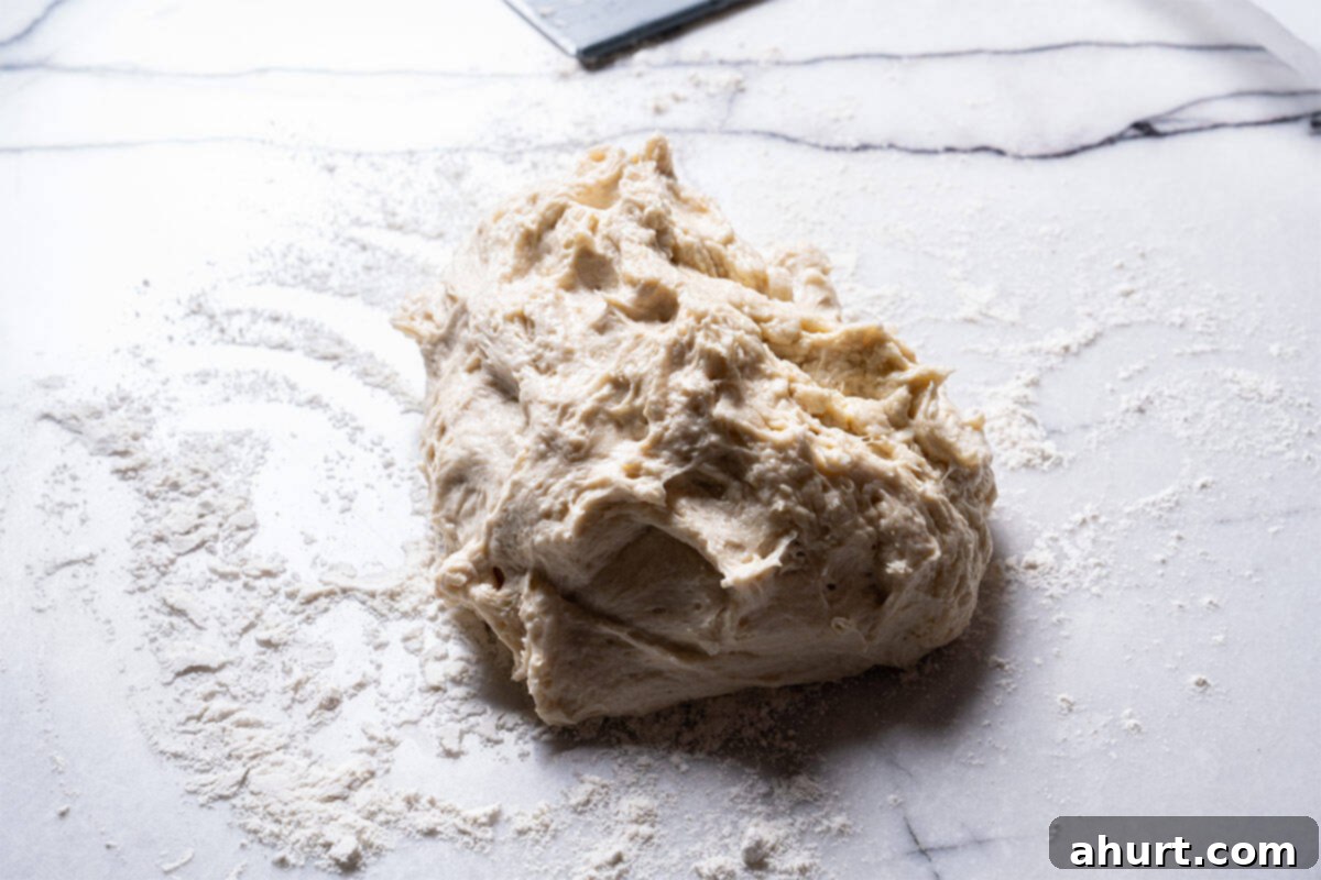 Effortless Artisan Crust: No-Knead Perfection 9 Dough is being scraped off the bowl and placed on the counter.