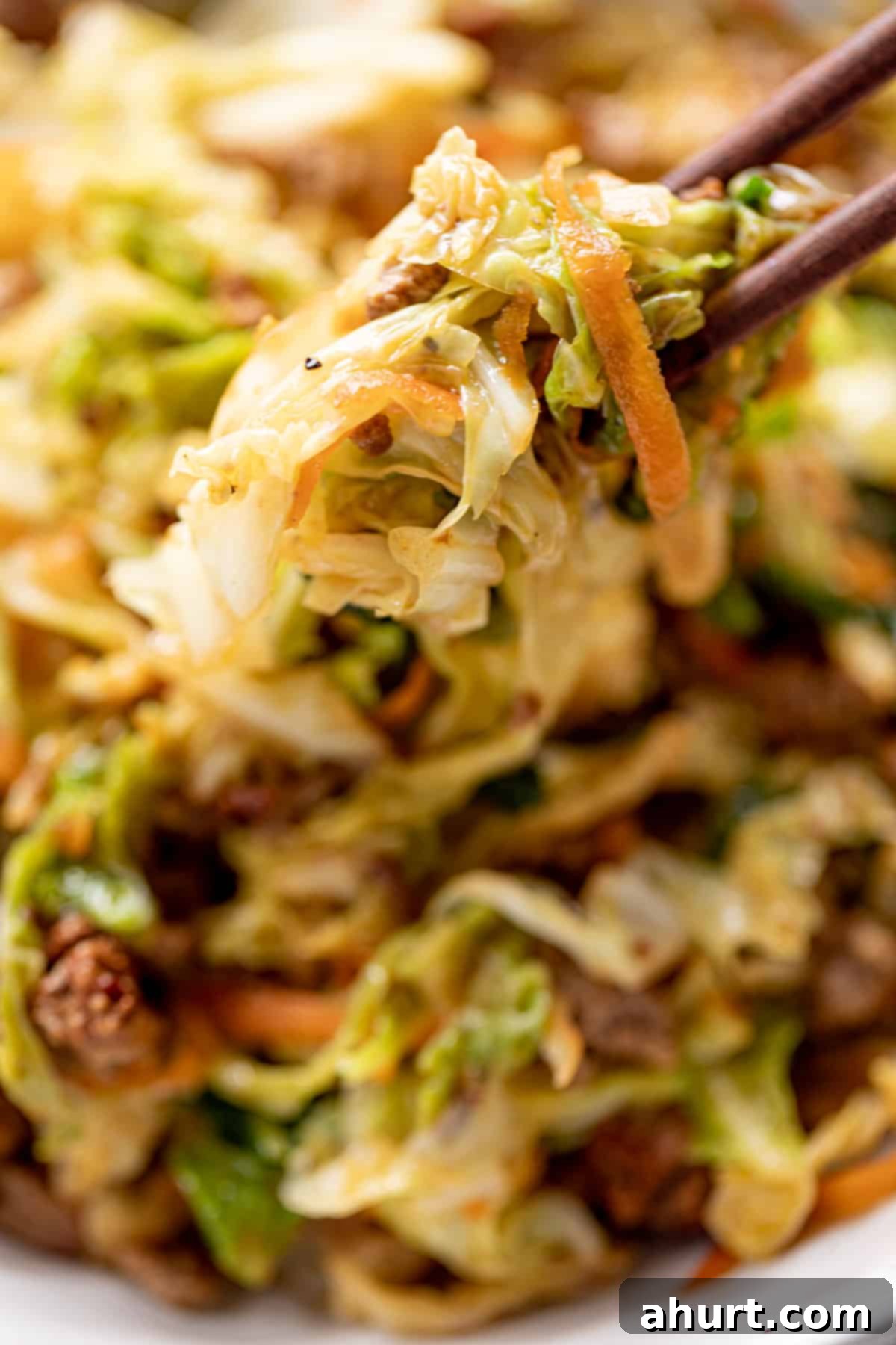 A close up image of chopsticks holding cabbage and ground beef. Emphasizes the appetizing nature of the dish.