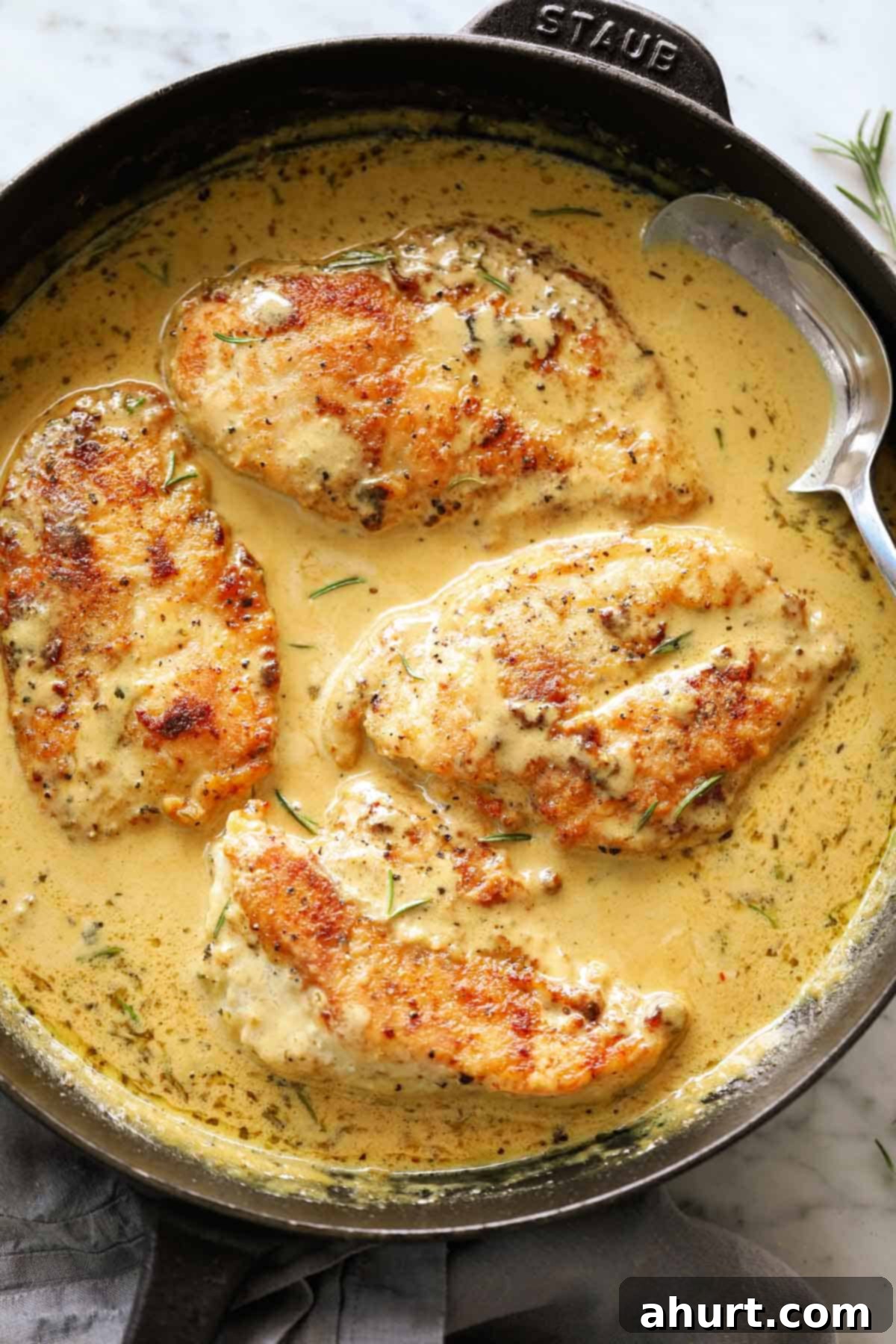Velvety Dijon Chicken 2 Creamy mustard chicken breasts in a black Staub skillet with a metal spoon, ready to be served.