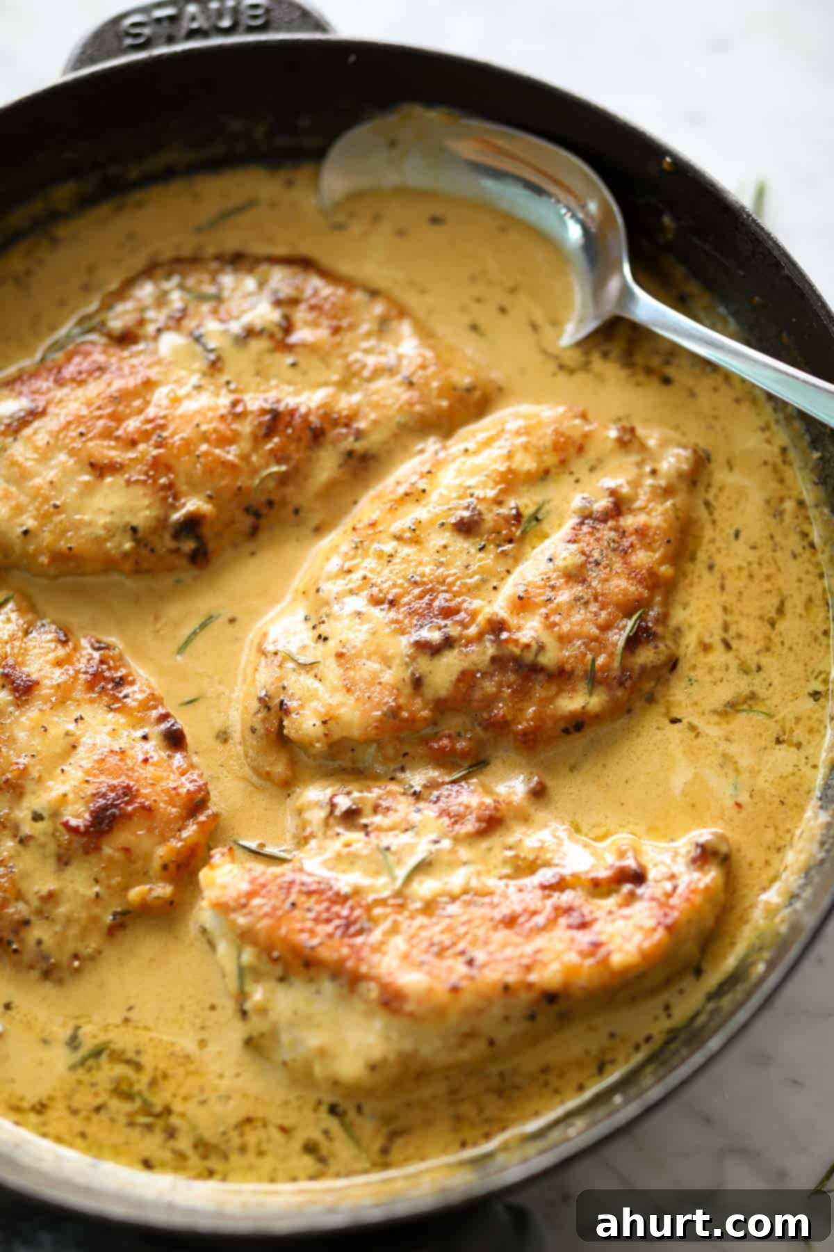 Velvety Dijon Chicken 5 Creamy mustard chicken breasts pieces in a black Staub skillet with a metal spoon, garnished with fresh tarragon.
