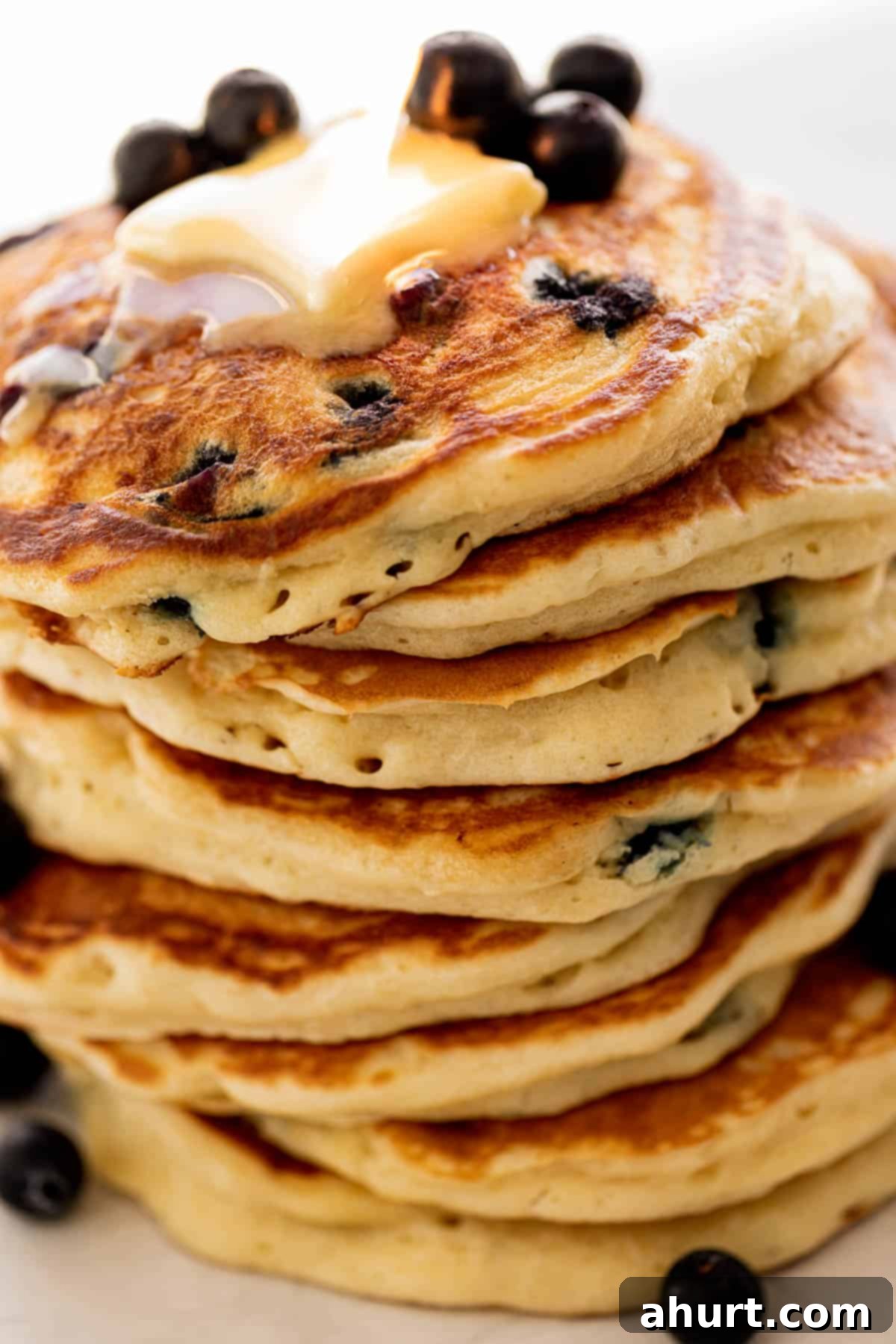 Morning Blueberry Bliss 2 Stacked fluffy blueberry pancakes on a plate, adorned with fresh blueberries and melted butter, ready to be enjoyed.
