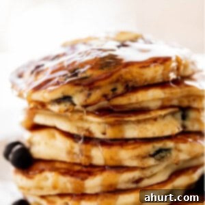 Morning Blueberry Bliss 9 A stack of Blueberry Pancakes on a plate with maple syrup. Topped with fresh blueberries.