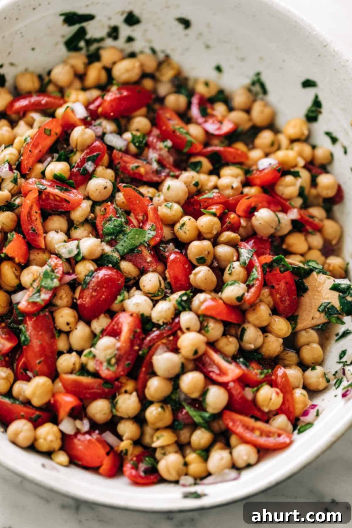 Mediterranean Chickpea Tomato Salad 8 Chickpea Tomato Salad mixed with a lemon herb dressing in a white bowl on a white marble table background.