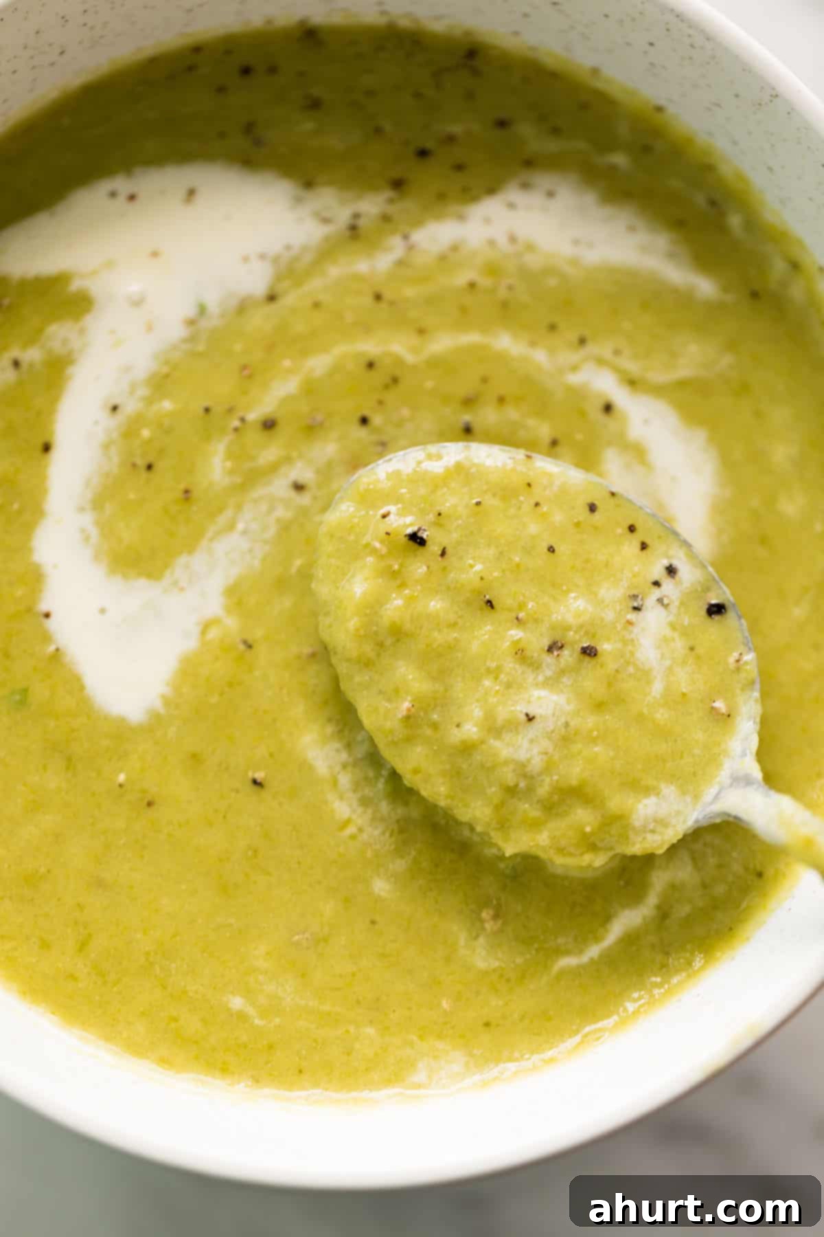 Velvet Asparagus Soup 2 A comforting white bowl of cream of asparagus soup garnished with cracked black pepper. Served with a silver metal spoon is ready to eat!